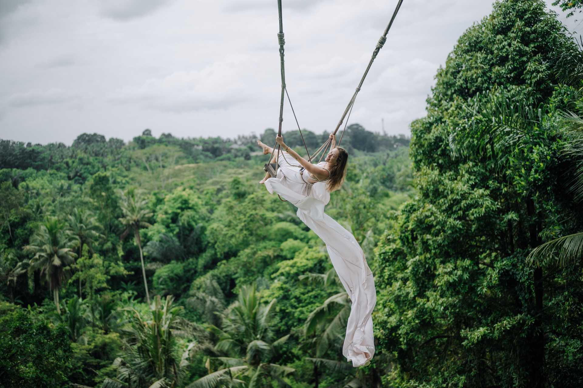 Guest on a jungle swing over the Ayung river valley with palm trees surrounding
