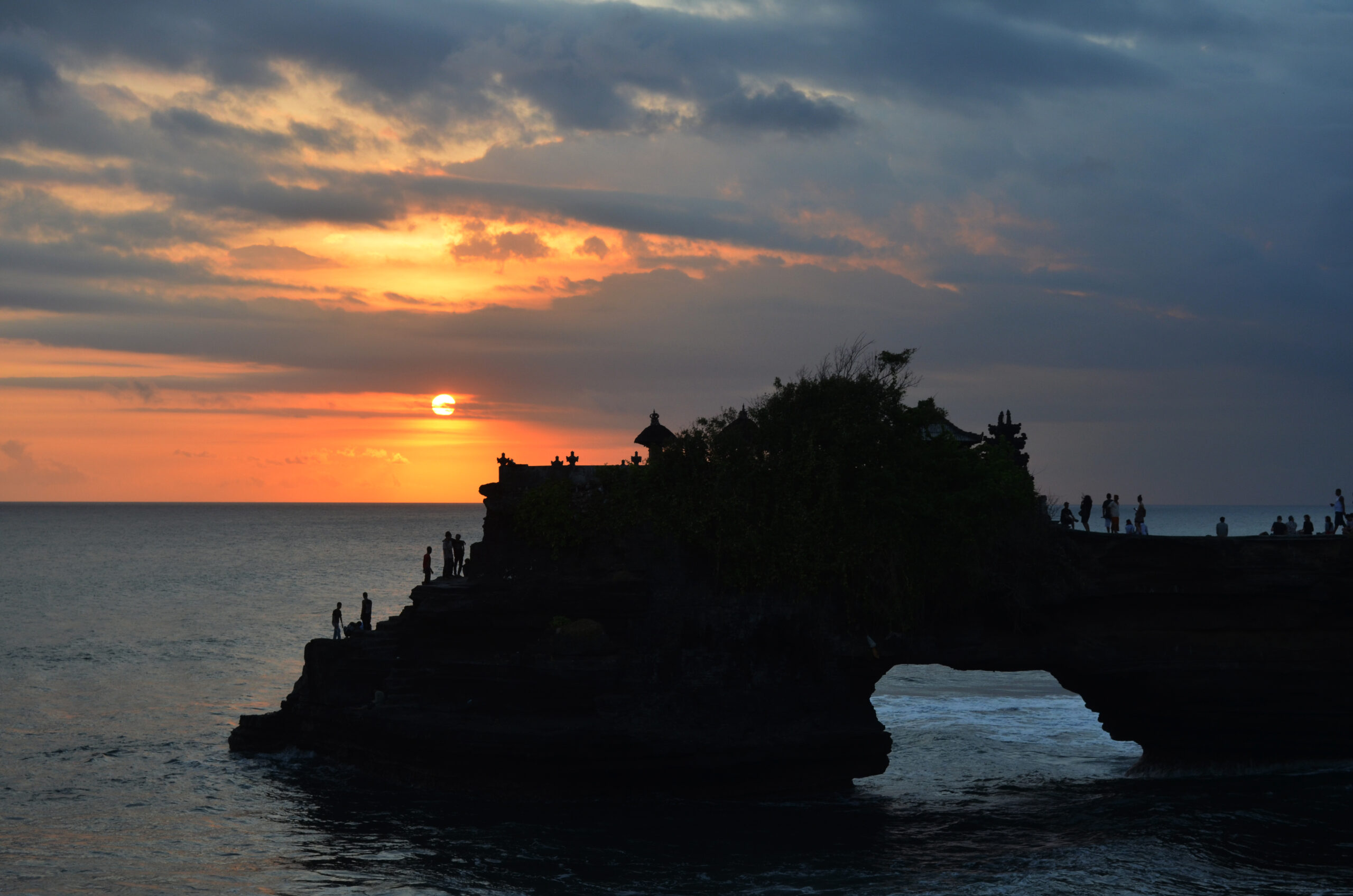 Tanah Lot sea temple silhouetted against the ocean at sunset with waves breaking on the base rock